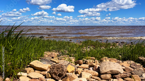Rocky Lakeshore with Green Grass and Dramatic Cloudscape Over Water