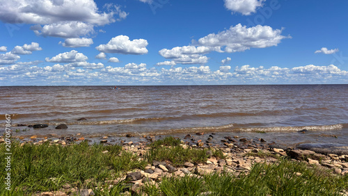 Rocky Lakeshore with Green Grass and Dramatic Cloudscape Over Water