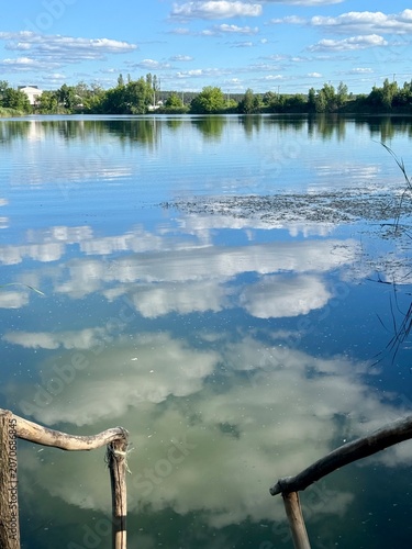 Fotografie Quiet forest lake with wooden stairs leading to the water, reflecting clouds and surrounding trees on a calm day