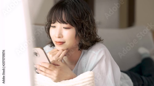 ソファに寝転んでスマートフォンを使う女性, Woman Using a Smartphone While Lying on a Sofa