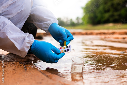 Researcher in protective gloves comparing litmus test paper color chart for acidity analysis.