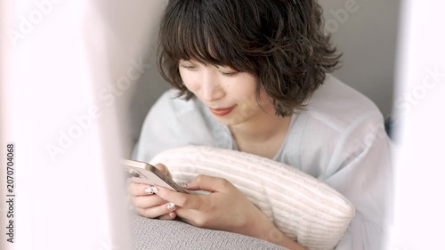 ソファに寝転んでスマートフォンを使う女性, Woman Using a Smartphone While Lying on a Sofa