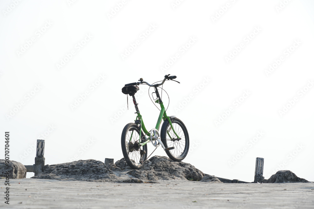 Fototapeta premium Green folding bicycle parked on a rocky surface against a bright.