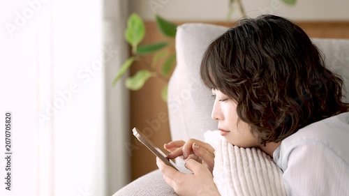 ソファに寝転んでスマートフォンを使う女性, Woman Using a Smartphone While Lying on a Sofa