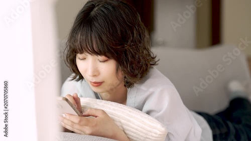 ソファに寝転んでスマートフォンを使う女性, Woman Using a Smartphone While Lying on a Sofa
