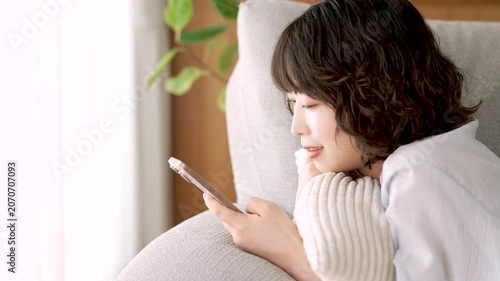 ソファに寝転んでスマートフォンを使う女性, Woman Using a Smartphone While Lying on a Sofa