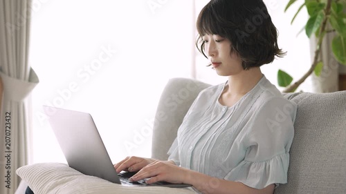 リビングのソファでノートパソコンを使う女性, Woman Using a Laptop on a Sofa in the Living Room