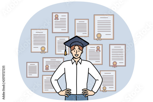 Man graduate stands in academic hat near wall with diplomas from advanced business courses. Guy is graduate and proud of good education and availability of documents confirming qualifications