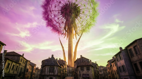 Giant dandelion towers above quaint townhouses. Soft pink and purple skies glow behind it. Its seeds drift upward as light filters through. Cobbled streets and aged rooftops frame the scene