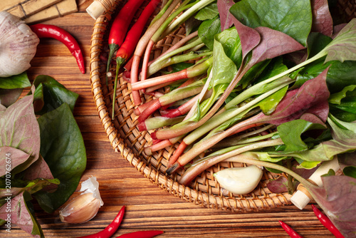 Foto Fresh leafy greens with garlic and red chilies in a woven basket on a wooden tab