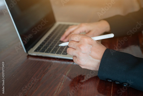 Close-up selective focus of a businessman holding a digital stylus pen with a blurred laptop in the background.