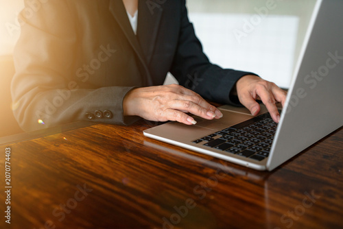 Close-up of a businessman typing on laptop computer on wooden table.