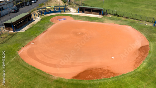 Tableau sur toile Aerial view of a perfectly groomed baseball infield diamond with vibrant red clay dirt, bordered by lush green grass and benches, alongside player dugouts and baseline markers under a bright day