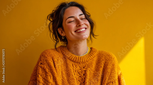 Happy young woman with closed eyes smiling in cozy orange sweater, portrait