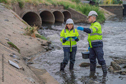 Environmental engineers collecting water samples for laboratory analysis and quality control monitoring near industrial drainage pipes to ensure safety and ecological sustainability standards.