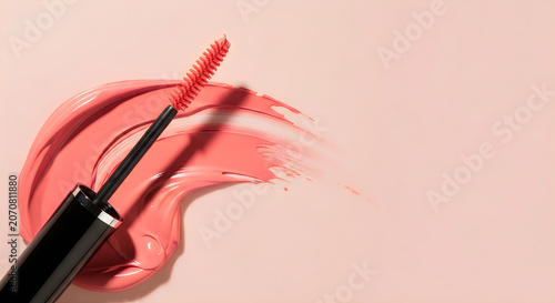 Pink mascara wand with coral color smear on light peach background