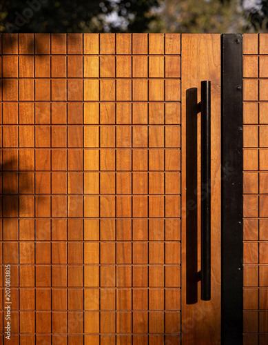 Modern wooden gate with black metal handle and grid pattern design