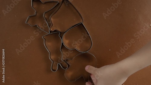 Mother and child hands press metal cutters into gingerbread dough on kitchen table. Family prepares homemade sweet chocolate cookie dessert shapes for holiday baking recipe lifestyle context.