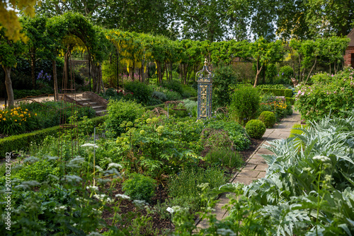 Obraz na płótnie A vibrant formal garden pathway at Kew botanical gardens with lush greenery, yellow laburnum arches, and decorative elements