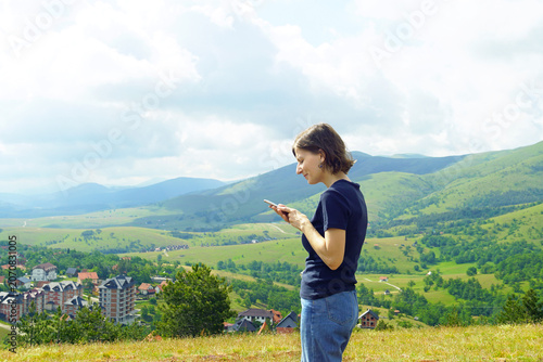 Cuadro en lienzo Woman viewing smartphone against mountain backdrop with settlements dispersed across green valley