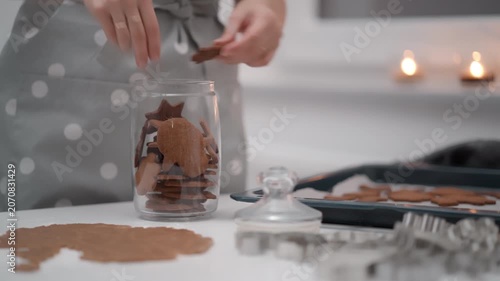 Woman fills a glass jar with baked gingerbread cookies and closes the lid. Housewife stores sweet homemade biscuit dessert finishing holiday baking recipe process in a domestic kitchen room.