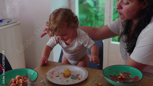 Photos Mother adjusting restless toddler at dining table guiding him into position to e