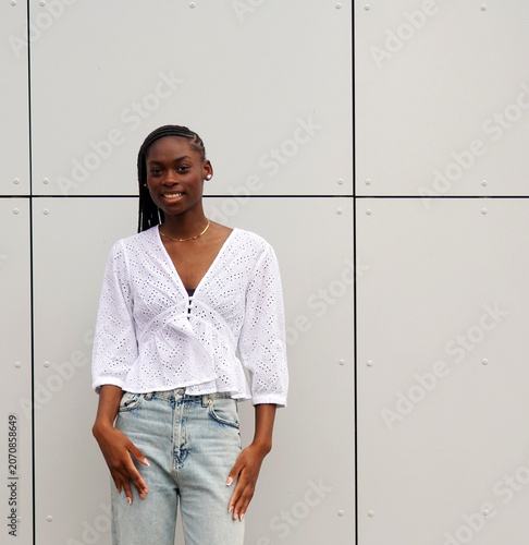 street style. beautiful afro woman smiling, with braided hairstyle, white Swiss embroidery openwork blouse and high-waisted light wash jeans. copy space