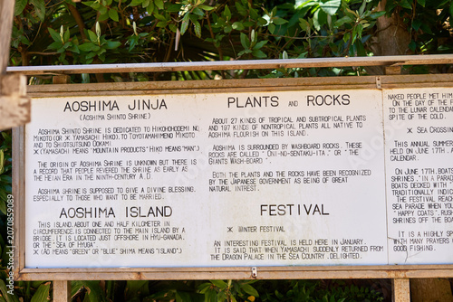 An informational signboard at Aoshima Jinja (Aoshima Shinto Shrine) in Miyazaki, Japan, displaying English text explaining the shrine's dedication to deities including Hikohohodemino Mikoto and
