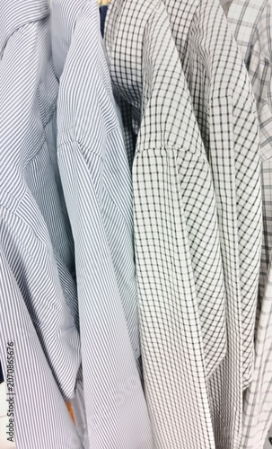 Striped and checkered men's shirts displayed on a clothing rack in a retail fashion store.