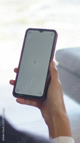 Vertical video: Adjusting person holding phone in purple case on sofa, responding to crosshair