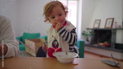 Fotografie Toddler eating snack from bowl at wooden table while concentrating on food, play