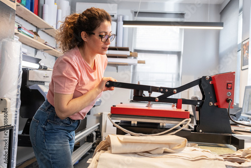 Bild auf Leinwand A print shop worker is operating a heat press machine for textile printing, carefully aligning the material before pressing