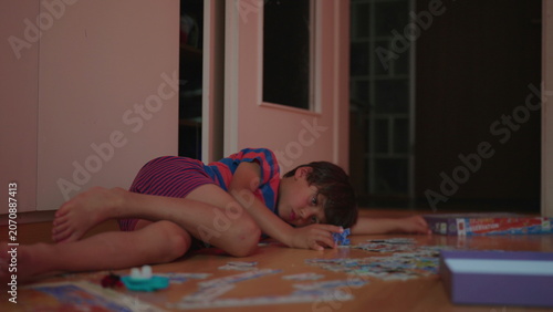 Photos Boy lying on floor surrounded by puzzle pieces looking tired and disengaged quie