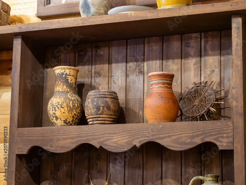Φωτογραφία A collection of vintage clay pottery jugs and a small woven wicker mat stand displayed on a rustic dark wooden cupboard shelf