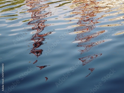 Fotografie Industrial tower silhouettes wavering across sunlit moving water