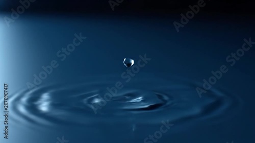 Single Crystalline Water Droplet Falling and Creating Circular Ripples in Calm Blue Water