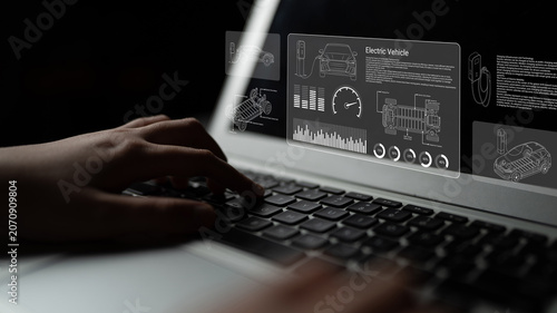 Bild auf Leinwand A close-up view of hands typing on a laptop displaying electric vehicle technology with graphics for motor specifications and data analysis in a digital interface
