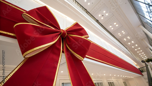 Low Angle Shot of Oversized Red Satin Ribbon Bow on Grand Building Interior Christmas Holiday Decoration Festive Architectural Display Luxury Mall Celebration Concept