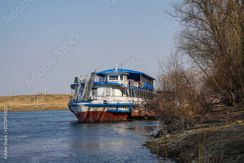 Passenger river vessel moored along quiet riverbank, inland waterway transportation and regional ferry service in rural landscape with copy space