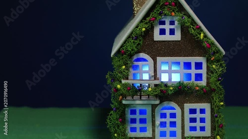 On a dark blue background and green covering, a fairytale decorated house with color-changing light in the windows