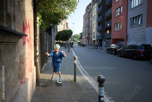 Young boy in helmet rides skateboard on sidewalk in European city street