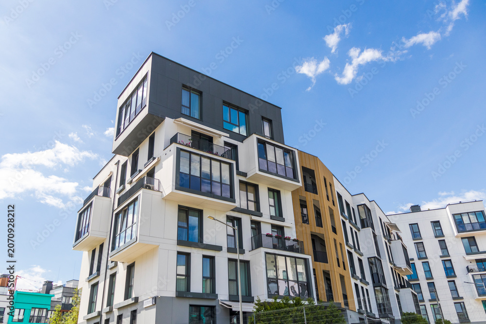 Fototapeta premium Modern apartment building facade with white and dark grey panels under blue sky. Urban