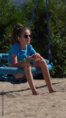 A teenage girl with an electronic key bracelet and sunglasses is relaxing in a hammock.