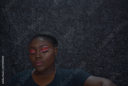 Portrait of a brown skin woman with red eyeshadow and white eyeliner with grey background, an African woman with bright red eye shadow white liner and a nude lip, brown skin woman with bright makeup