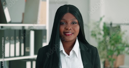 Portrait of African American woman in office shows confident smile and formal style. Businesswoman faces camera as presents professional workplace image