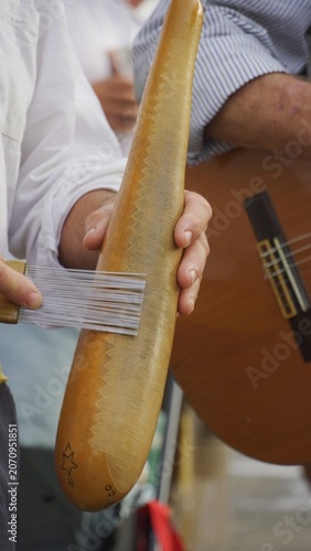 Musician playing traditional güira percussion instrument with a comb scraper, performing folk music during a pilgrimage celebration in the Canary Islands