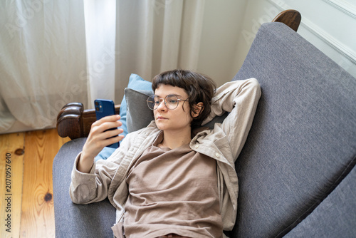 Cuadro en lienzo Lazy woman browsing social media on smartphone while lounging on sofa