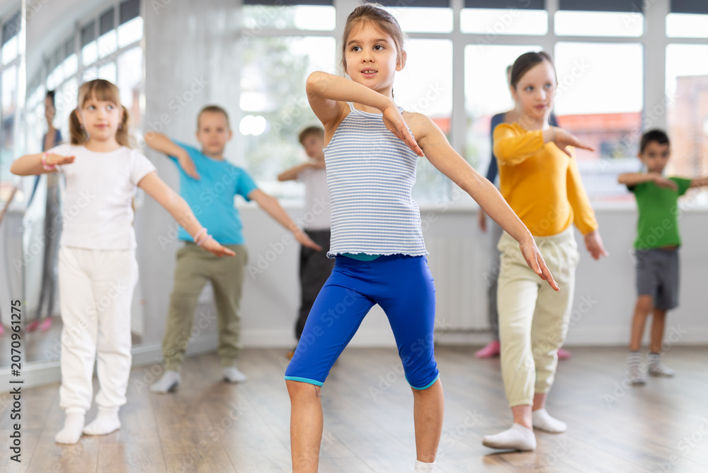 Fototapeta premium Girls with boys repeat teaches sequences of movements during training, train to perform electro dance, enjoys active hobby to favorite music. Unrecognizable female teacher administer conduct class