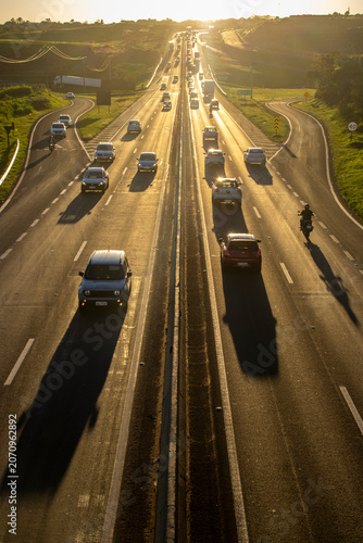 Marilia, SP, Brazil, November 19, 2025. Highway SP-294 in Marilia, at sunset. Intense traffic of cars and trucks flows through the green landscape, illuminated by the golden hour light.