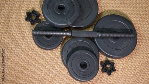 Disassembled black dumbbell weight set on floor. Disassembled black dumbbell with various weight plates lying on a textured brown floor, highlighting home gym equipment for strength training
